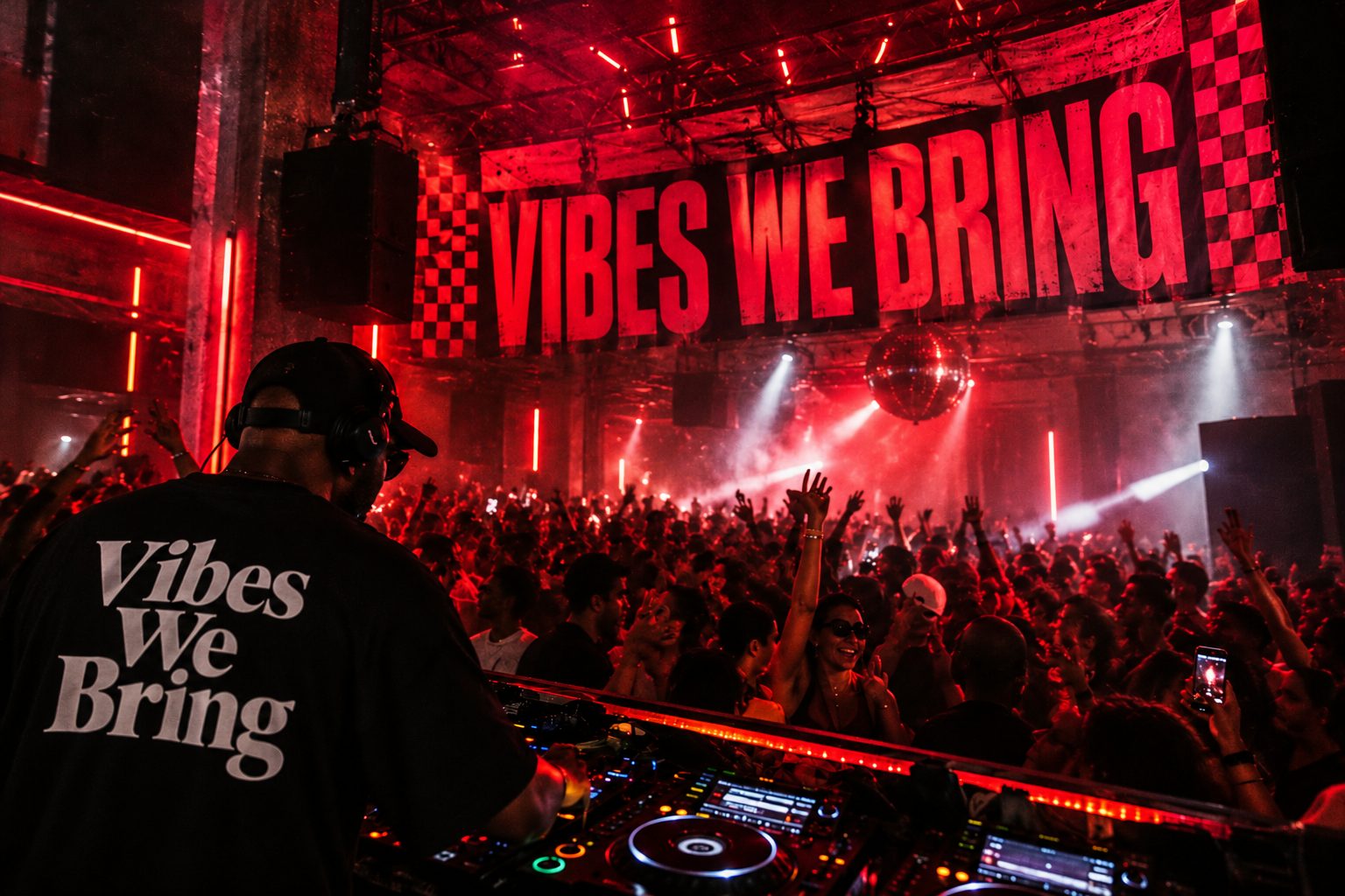 A DJ in a cap and headphones, seen from behind in a black T-shirt printed Vibes We Bring, mixing on CDJs in front of a packed, red-lit crowd with hands in the air, a mirror ball and a large Vibes We Bring banner with checkerboard edges.